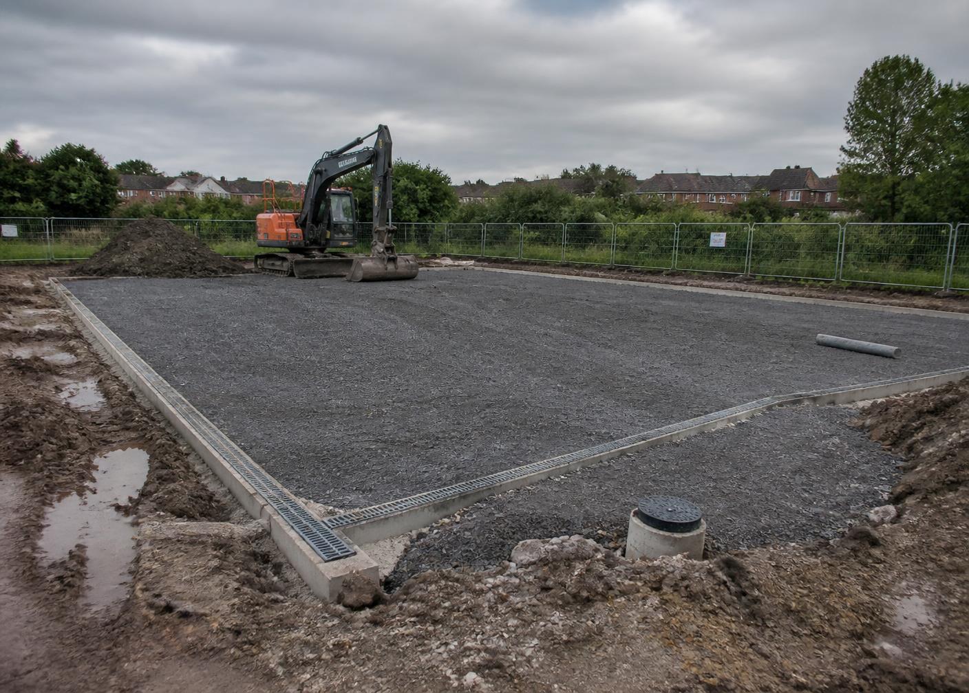Groundworks in progress for a sports court base with stone sub-base and drainage channel