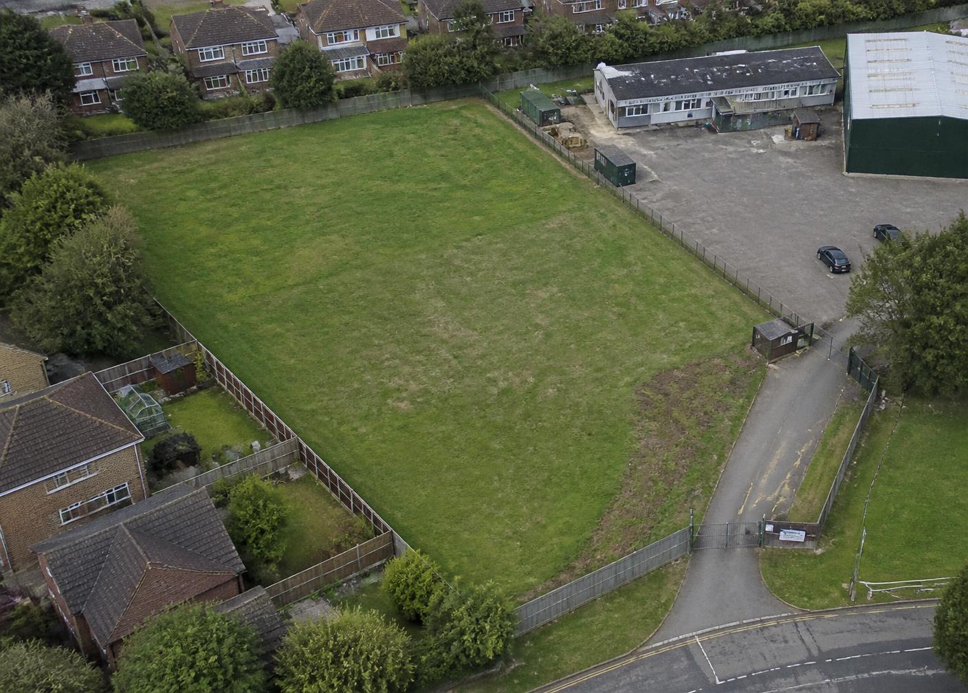 Aerial view of a UK plot of land with access road, boundary fencing and neighbouring houses